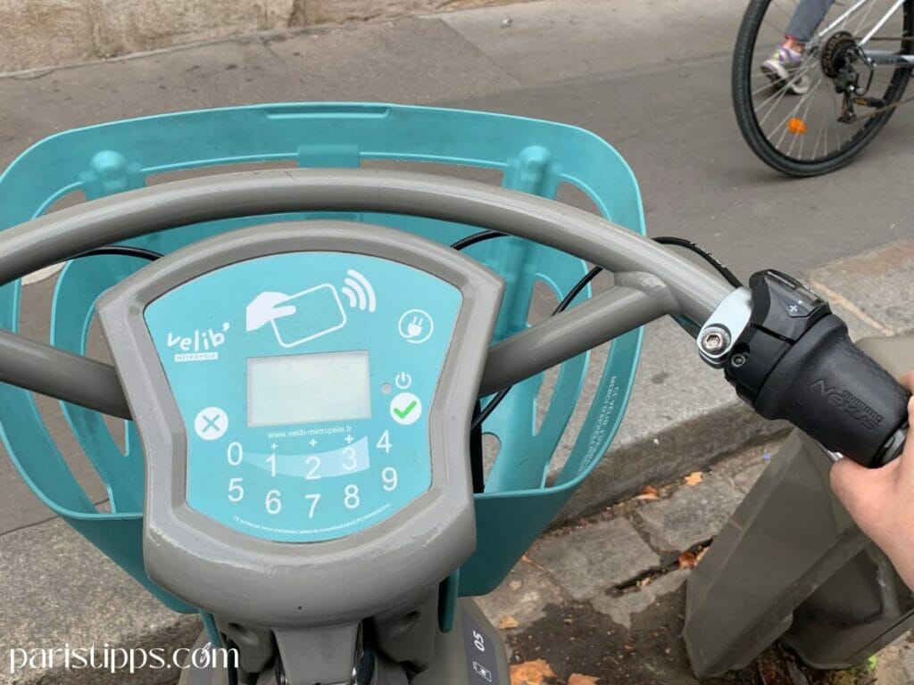 V-Box am Lenker eines Vélib E-Bikes in Paris mit Display und Tastatur zur Eingabe des Zugangscodes. Über dieses System wird das Fahrrad entsperrt und die Nutzung gestartet. Ein wichtiger Teil der Velib Paris Anleitung für Touristen.