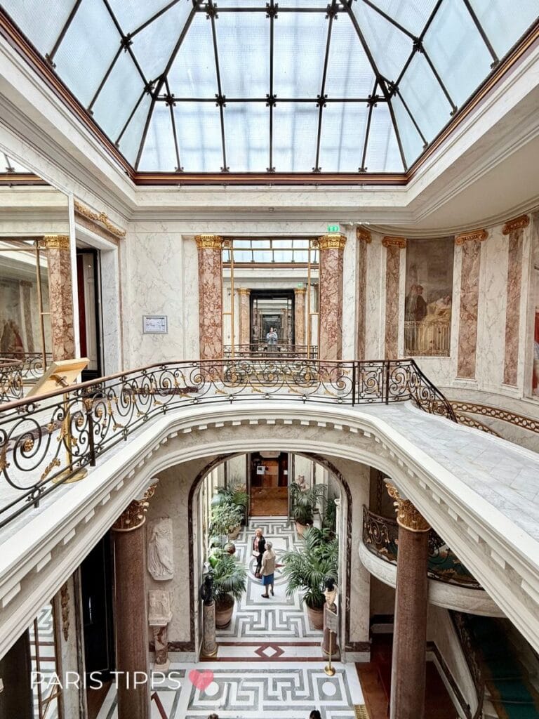 Wintergarten im Musée Jacquemart-André in Paris: Blick auf das elegante Treppenhaus mit Marmor, Palmen und Glasdach – ein Highlight der Belle Époque.