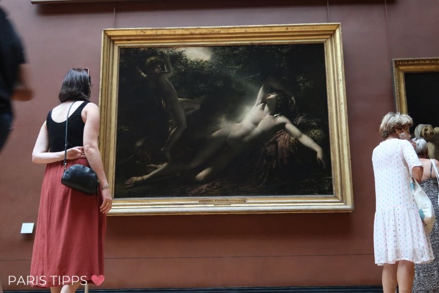 Lena Steht mit dem Rücken zur Kamera und blickt auf ein Gemälde im Louvre.