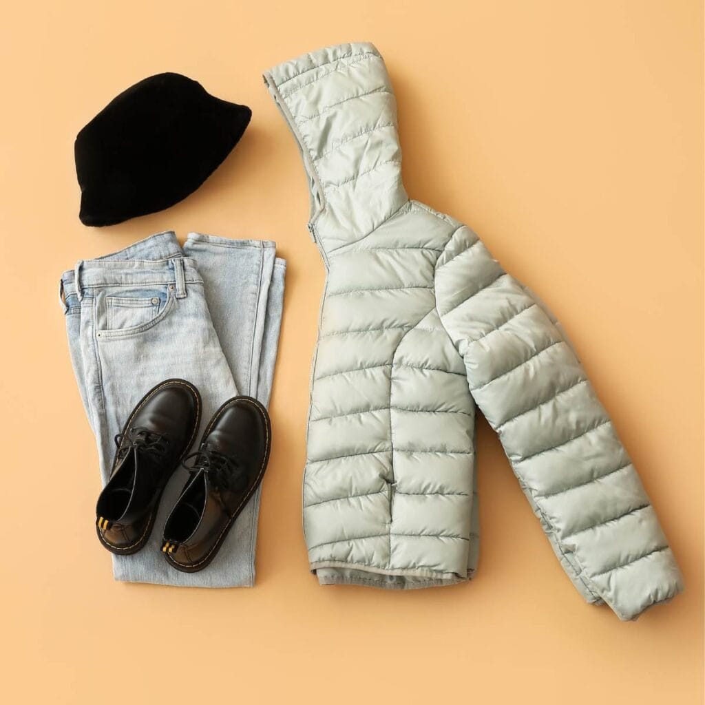Flach gelegte Winterkleidung für Paris: Daunenjacke, Jeans, schwarze Schuhe und eine schwarze Baskenmütze.