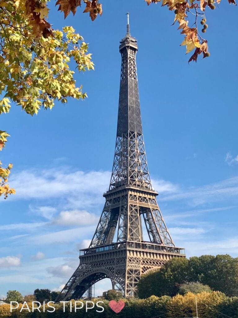 Eiffelturm ragt vor blauem Himmel empor und wird von herbstlichen Blättern eingerahmt. Unten steht "PARIS TIPPS ♥" und hebt dieses ikonische Paris Sehenswürdigkeiten Wahrzeichen hervor.