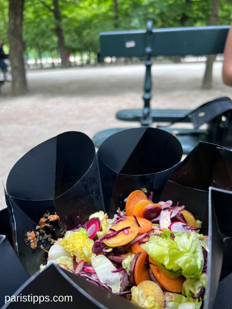Restaurants in Paris bieten ihre gerichte auch zum Mitnehmen an, wie hier Pierre Sang Express. Gericht mit Reis und Möhren in schwarzer schachtel, im Hintergrund ein Park und eine BAnk
