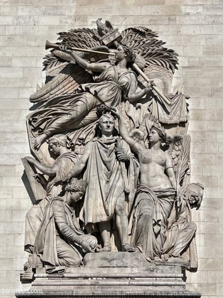 Steinrelief am Triumphbogen in Paris mit Napoleon im Zentrum, umgeben von allegorischen Figuren und geflügelter Siegesgöttin.