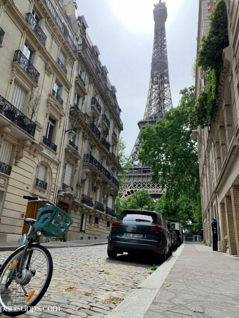 Vélib Fahrrad in einer ruhigen Straße nahe dem Eiffelturm in Paris. Das Fahrrad steht auf Kopfsteinpflaster mit Blick auf eines der bekanntesten Wahrzeichen der Stadt. Perfektes Beispiel für Fahrradfahren in Paris abseits der großen Verkehrsachsen.