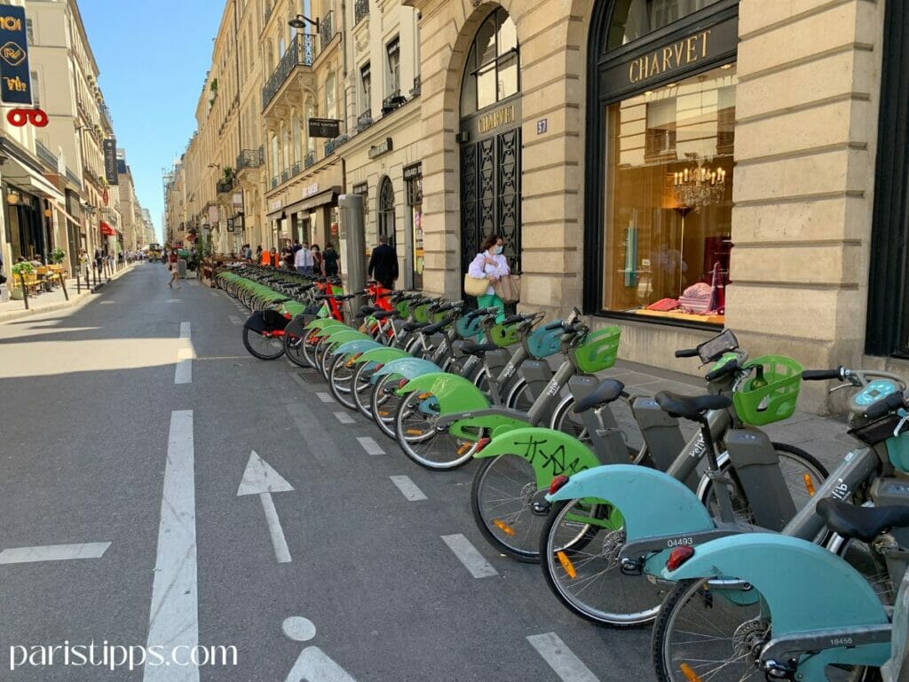 Vélib Fahrradstation in Paris mit vielen grünen und blauen Leihrädern entlang einer typischen Pariser Straße. Der Fahrradverleih Velib ist eine der beliebtesten Möglichkeiten, um sich flexibel durch die Stadt zu bewegen. Solche Stationen sind überall verteilt und machen Fahrrad mieten in Paris besonders einfach.
