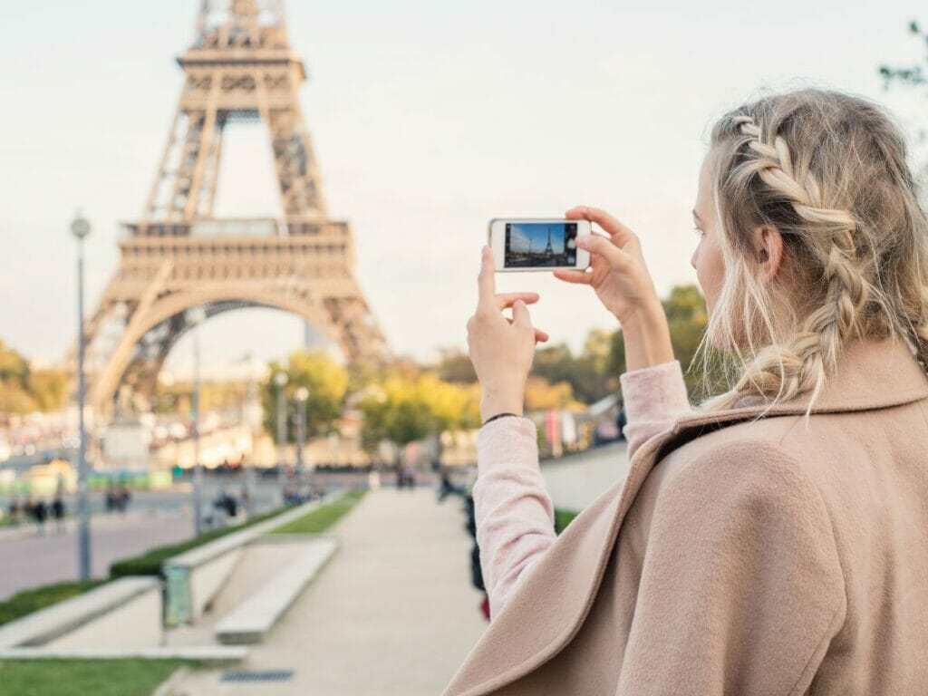  blonde teenager steht am Eiffelturm in Paris und macht Foto