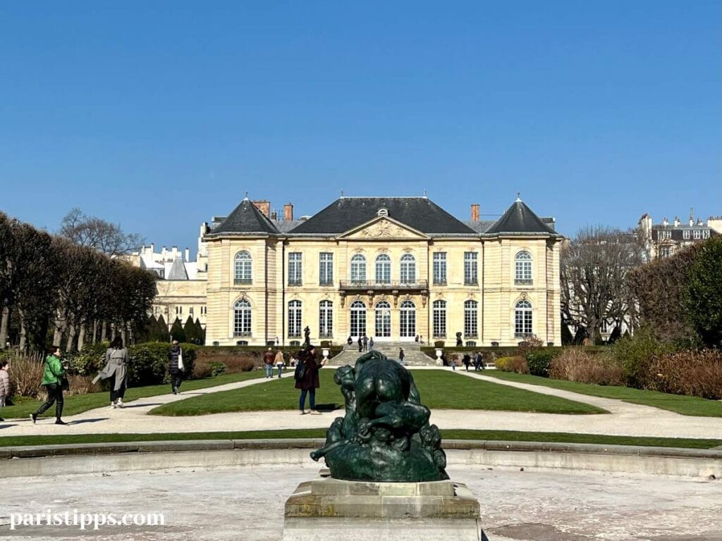 Hôtel Brilon an einem sonnigen Wintertag, mit Bäumen links und recht und einer Skulptur im Vordergrund.