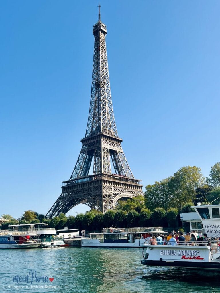 Der Eiffelturm bei blauem Himmel und die Seine mit einem Bateau Mouches im Vordergrund