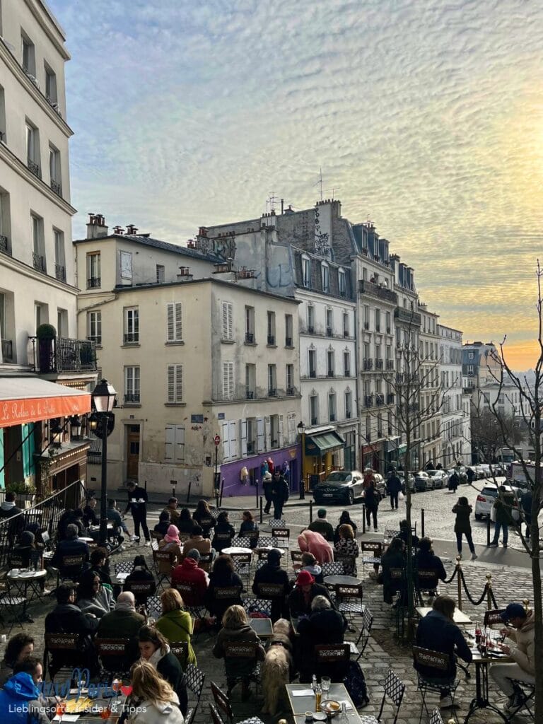 Releis de la butte Montmartre im Sonnenuntergang und vielen Menschen auf der Terrasse. Häuser im Hintergrund.