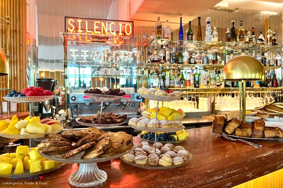 Bar mit Flaschen im Hintergrund und Tellern mit Gebäck und Obst im Vordergrund