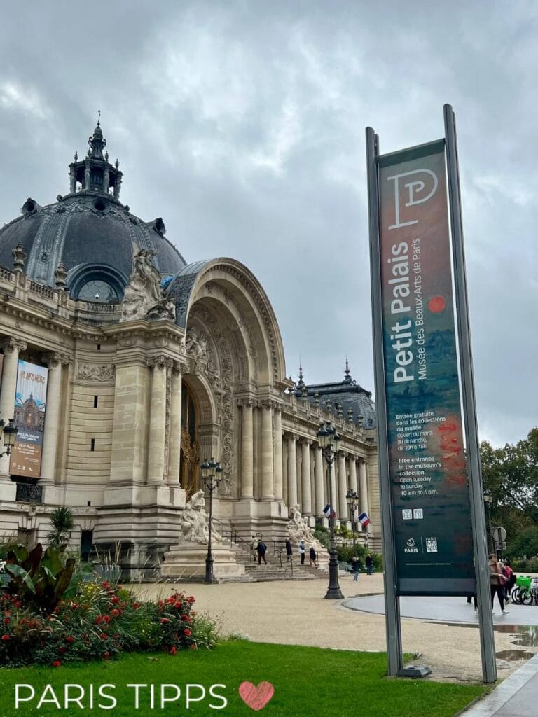 Außenansicht des Petit Palais in Paris mit prächtiger Architektur, einer goldenen Eingangstür und einem Infoschild, das auf die kostenlosen Dauerausstellungen und die Öffnungszeiten hinweist. Im Vordergrund ist ein gepflegter Garten mit Blumen zu sehen.