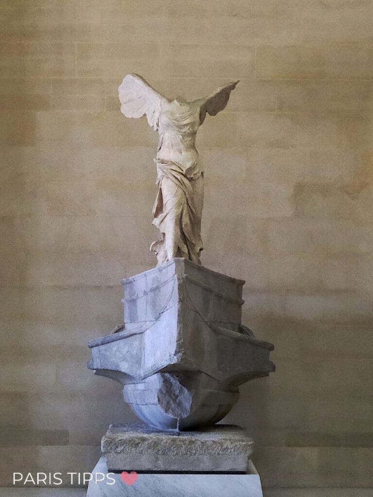 Große Galerie im Louvre mit gewölbter Glasdecke und langen Reihen klassischer Gemälde an den Wänden. Zahlreiche Besucher sitzen und gehen durch den Saal, der Teil des Rundgangs nach dem eintritt louvre ist, und unten links steht "PARIS TIPPS ❤️".