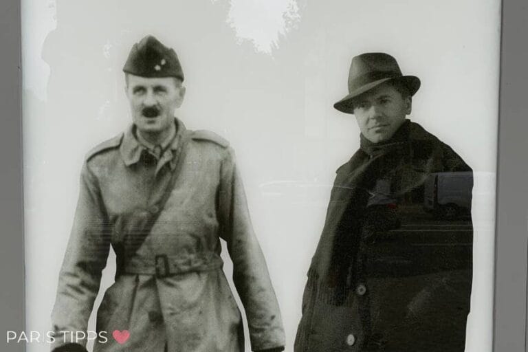 Schwarz-Weiß-Bild von zwei historischen Persönlichkeiten, General Leclerc in Militäruniform und Jean Moulin in einem Mantel und Hut, dargestellt auf einem Schild vor dem Musée de la Libération de Paris. Unten links ist die Aufschrift 'Paris Tipps' mit einem rosa Herz zu sehen.